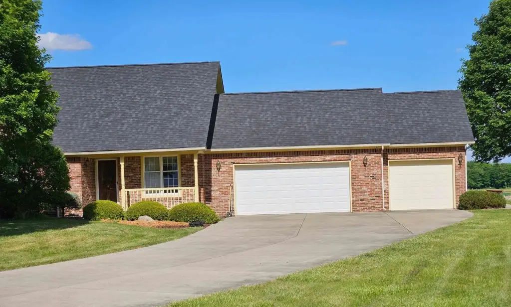 Brick house with gray roof and attached two-car garage; driveway in foreground, green lawn and trees.