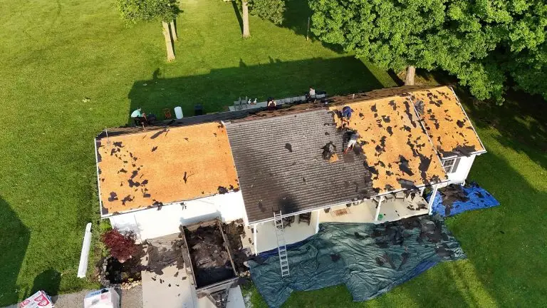 Aerial view of a house with damaged roof and tarps on the lawn.
