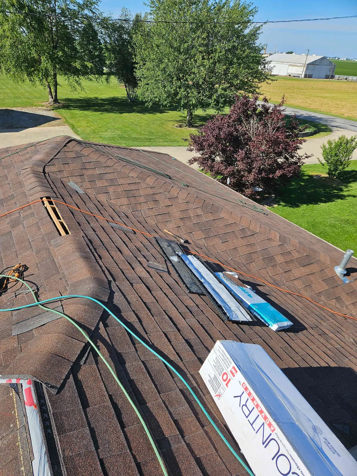 Rooftop with roofing materials and tools, green cable, and trees in background under a sunny sky.