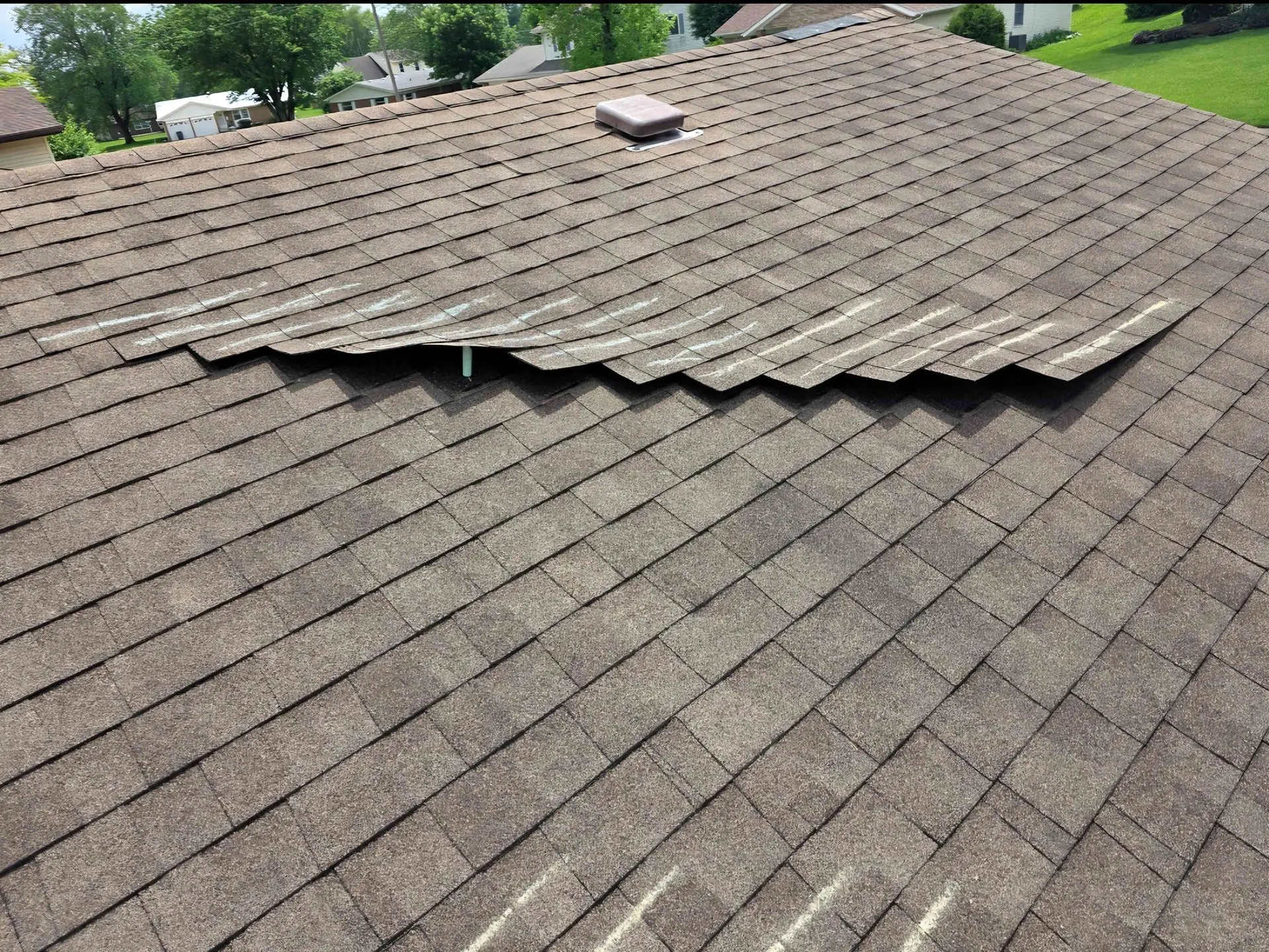 Brown asphalt shingle roof with a section of shingles buckling upwards, likely due to damage.