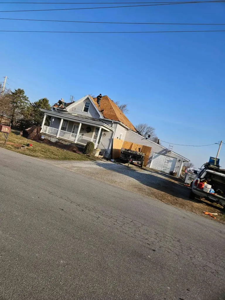 Old weathered house with a porch beside a road under a blue sky.