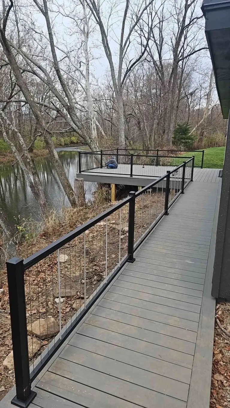Deck with black railing extends over a body of water. Trees in the background.